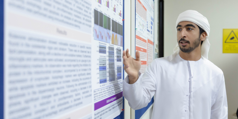 A student in Emirati dress presenting a scientific research poster with data and charts.